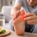 Seseorang sedang memijat jempol kaki yang nyeri sebagai gejala asam urat setelah lebaran 2026