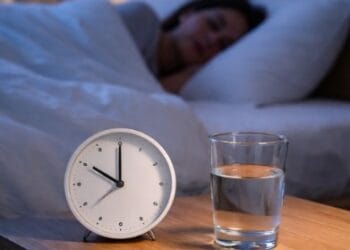 Ilustrasi jam weker di samping tempat tidur sebagai simbol jadwal tidur yang benar untuk diet