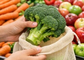 Seorang pria sedang memilih sayuran segar di supermarket sebagai tips belanja bahan makanan sehat