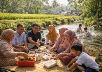 Keluarga besar piknik bersama di tepi sungai desa yang asri saat libur lebaran