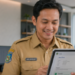 PPPK Daftar CPNS 2026, Foto pegawai pemerintah berseragam dinas sedang membaca dokumen persetujuan digital dengan ekspresi bahagia di dalam ruang kerja yang terang,
