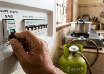 Seseorang sedang melakukan tips mengamankan instalasi listrik dengan mematikan saklar utama MCB untuk mencegah arus pendek saat gempa.