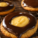 Visualisasi menggiurkan dari Resep Boston Cream Pie Cookies yang memperlihatkan tekstur kue empuk dengan isian krim vanilla dan siraman cokelat mengkilap.
