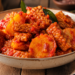 Foto sajian tempe dan kentang bumbu balado pedas mengkilap di dalam mangkuk keramik di atas meja kayu tradisional,