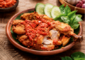 Sajian sepiring ayam penyet dengan lumuran sambal ulek merah yang segar dan lalapan hijau di salah satu rumah makan ayam penyet di Medan