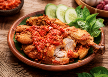 Sajian sepiring ayam penyet dengan lumuran sambal ulek merah yang segar dan lalapan hijau di salah satu rumah makan ayam penyet di Medan