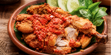 Sajian sepiring ayam penyet dengan lumuran sambal ulek merah yang segar dan lalapan hijau di salah satu rumah makan ayam penyet di Medan