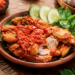 Sajian sepiring ayam penyet dengan lumuran sambal ulek merah yang segar dan lalapan hijau di salah satu rumah makan ayam penyet di Medan
