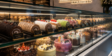 Jajaran bolu gulung cokelat dan roti manis yang terpajang rapi di dalam lemari kaca salah satu toko kue di Medan