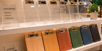 Jajaran papan ujian akrilik transparan tebal untuk kantor dan alat clipboard dada bahan kayu minimalis yang tersusun sangat rapi di dalam etalase toko perlengkapan stasioneri