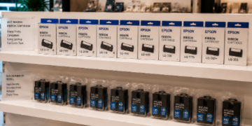 Jajaran tempat pita printer model ribbon cartridge hitam tebal untuk mesin kasir dan alat isi ulang pita cetak nilon minimalis yang tersusun sangat rapi di dalam etalase toko perlengkapan kantor
