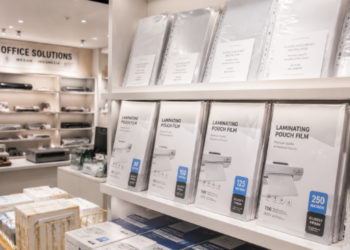 Jajaran tempat plastik laminating bahan poliester jernih untuk pengaman dokumen dan alat laminating pouch film minimalis berbagai ukuran mika yang tersusun sangat rapi di dalam etalase toko perlengkapan kantor