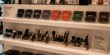 Jajaran tempat bak stempel meja berbahan akrilik mewah dan wadah tinta cap minimalis yang tersusun sangat rapi di dalam etalase toko perlengkapan kantor