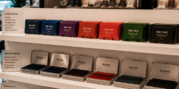 Jajaran bak stempel meja model wadah tertutup bahan plastik tebal dan alat bantalan cap flash otomatis warna-warni yang tersusun sangat rapi di dalam etalase toko perlengkapan kantor